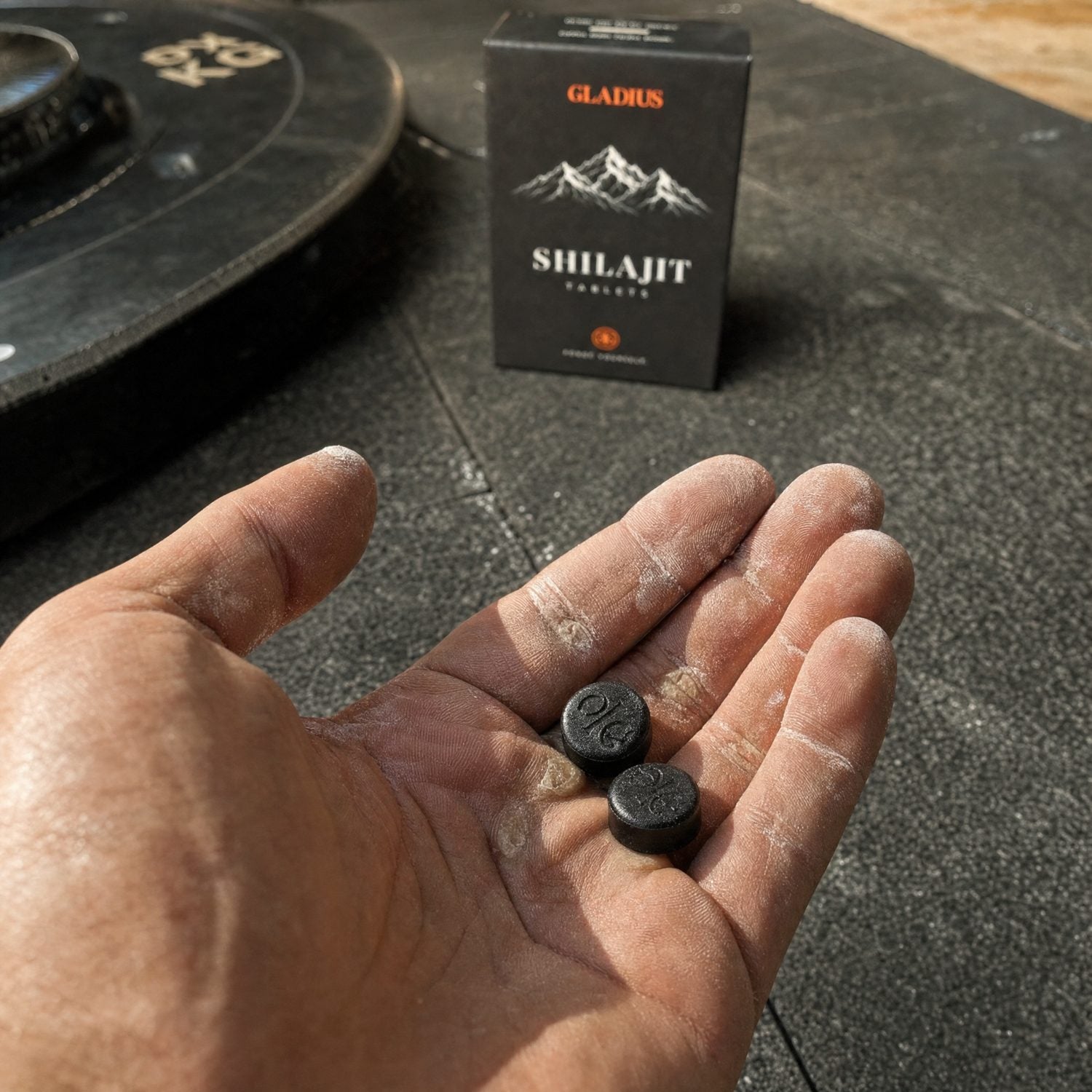 Two black shilajit tablets in a chalked palm at the gym